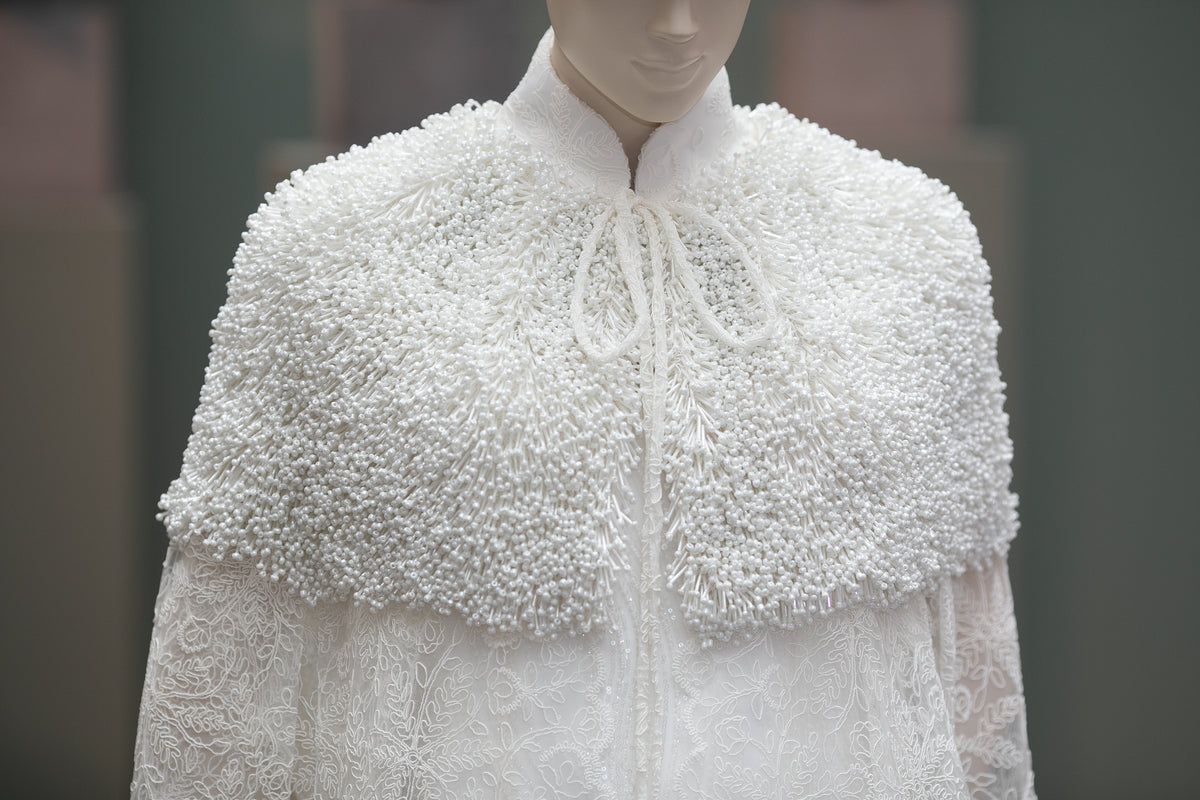 Cape longue en dentelle blanche de la Collection 2026 LYSANDRE PARIS, avec épaules entièrement brodées de longues perles tubulaires et de petites perles rondes.